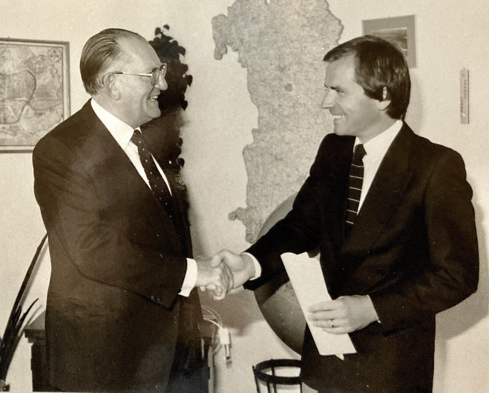 Zwei Männer schütteln sich vor einer Landkarte die Hände