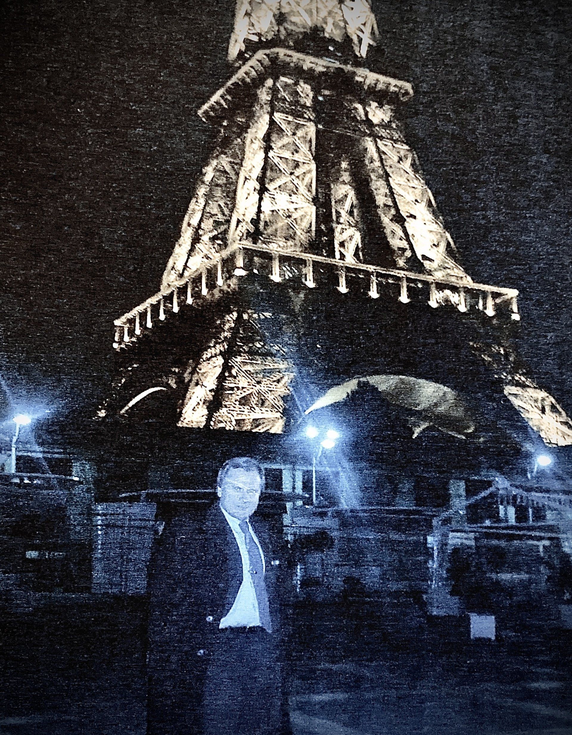 Ein Mann steht nachts vor dem Eiffelturm