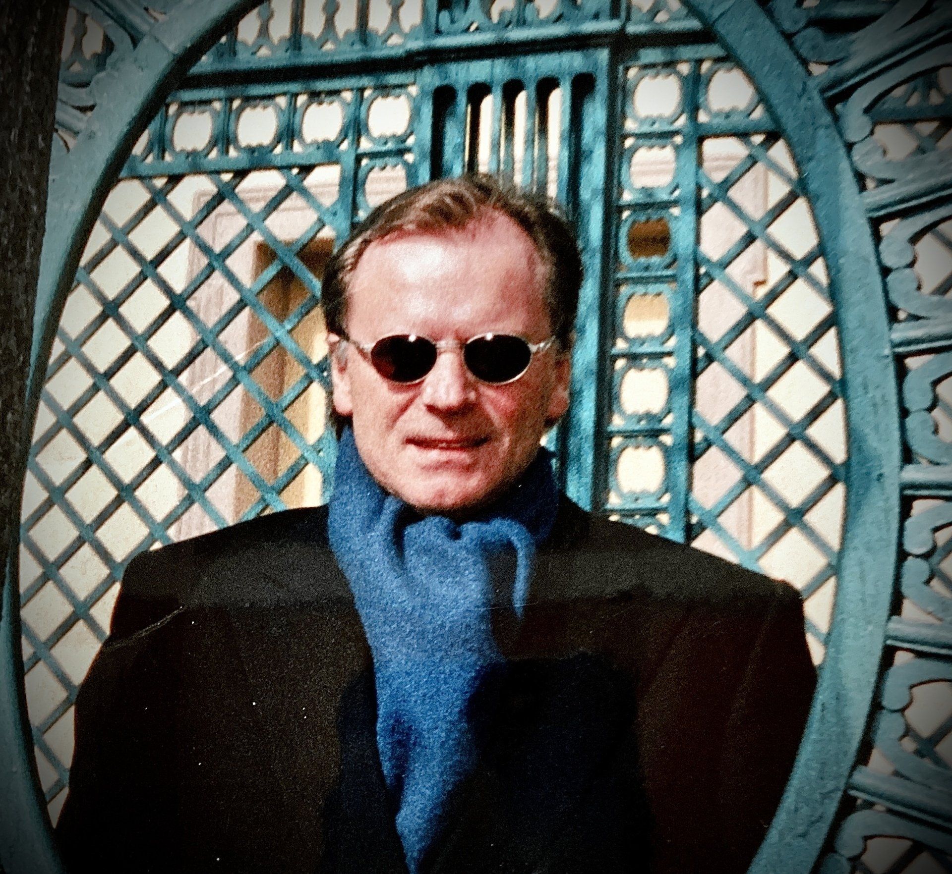 Ein Mann mit Sonnenbrille und blauem Schal steht vor einem blauen Zaun