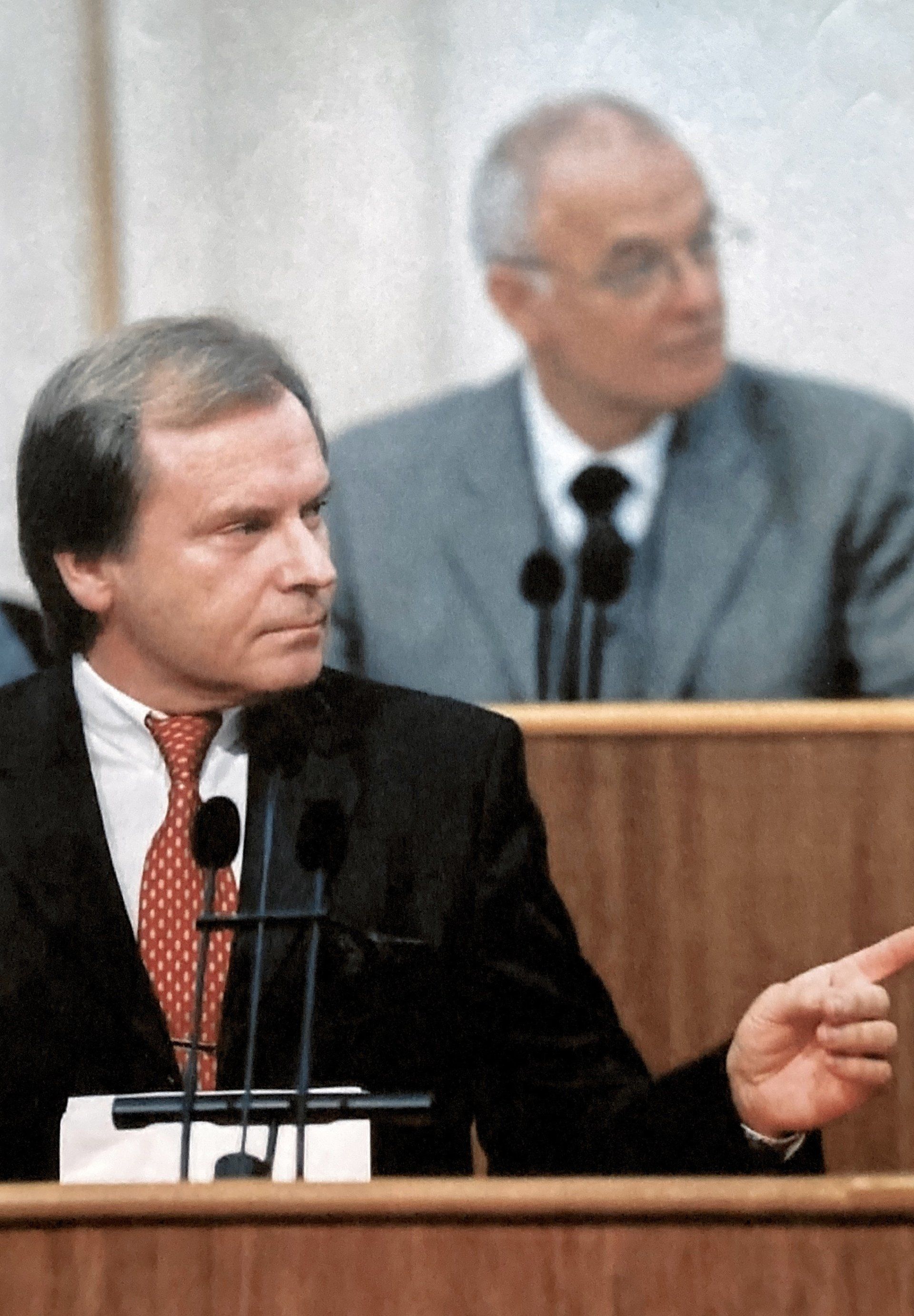 Ein Mann in Anzug und Krawatte hält eine Rede vor Mikrofonen