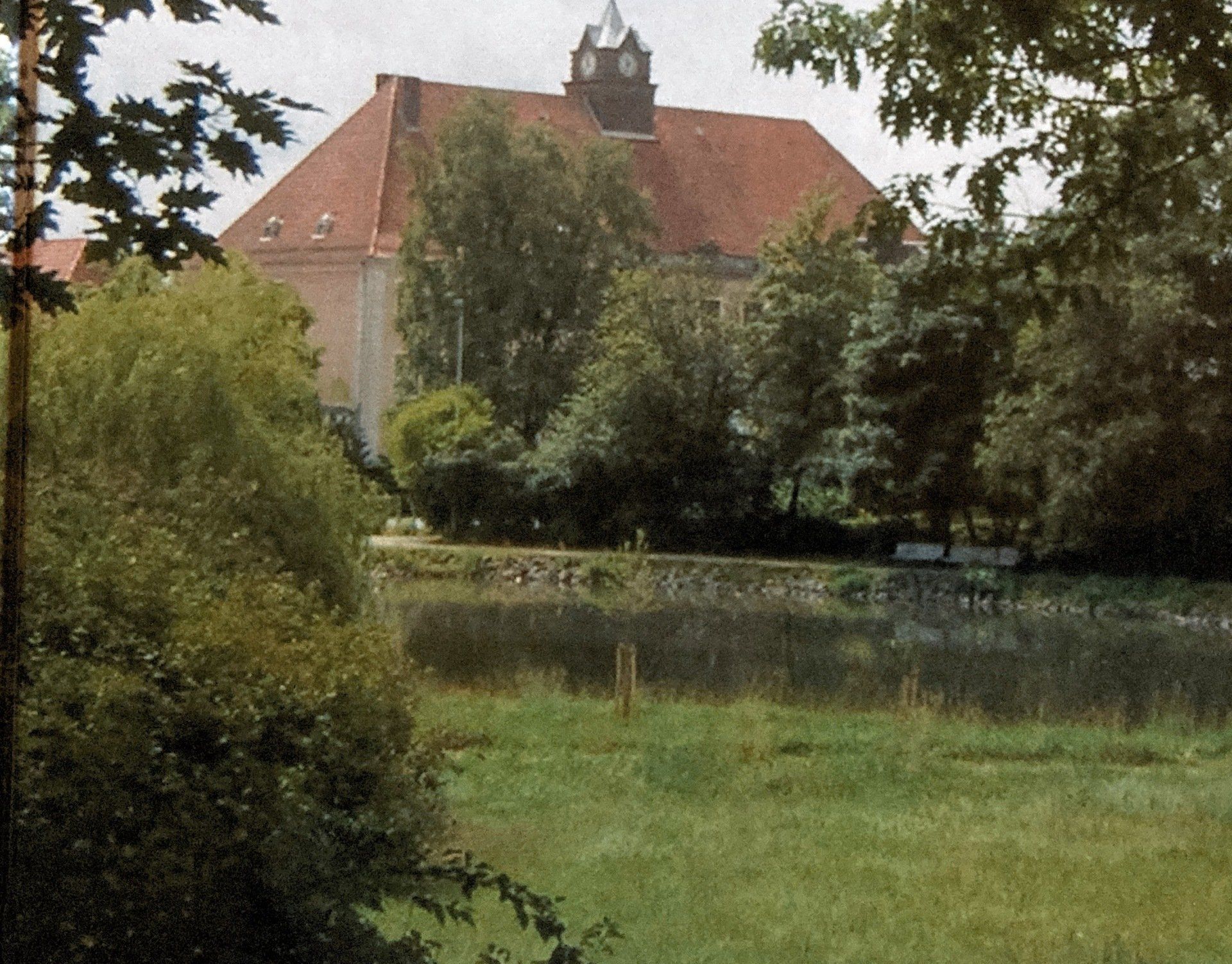 Hinter einem See liegt ein großes Gebäude mit einem Uhrturm