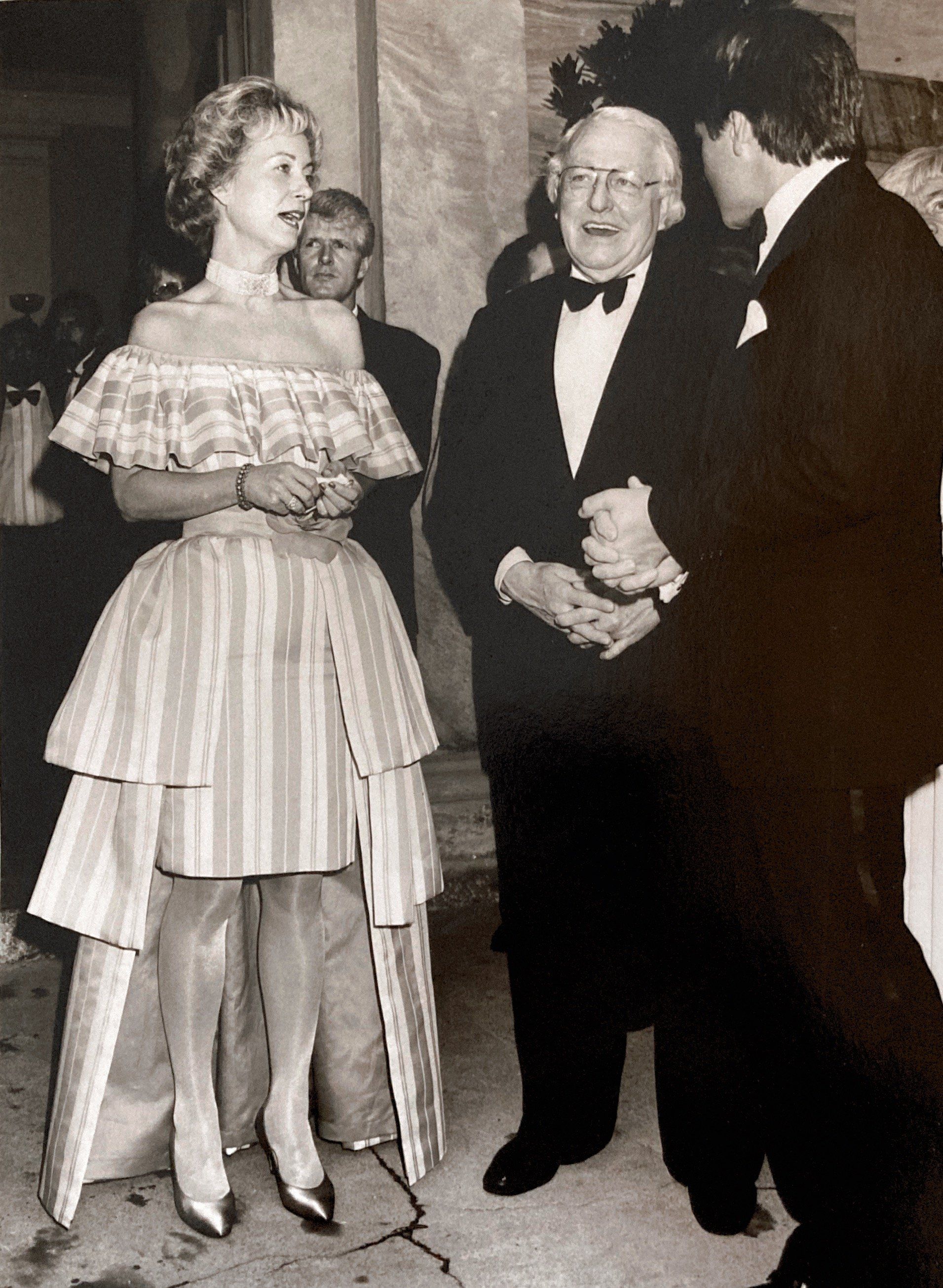 Eine Frau in einem gestreiften Kleid spricht mit zwei Männern im Smoking