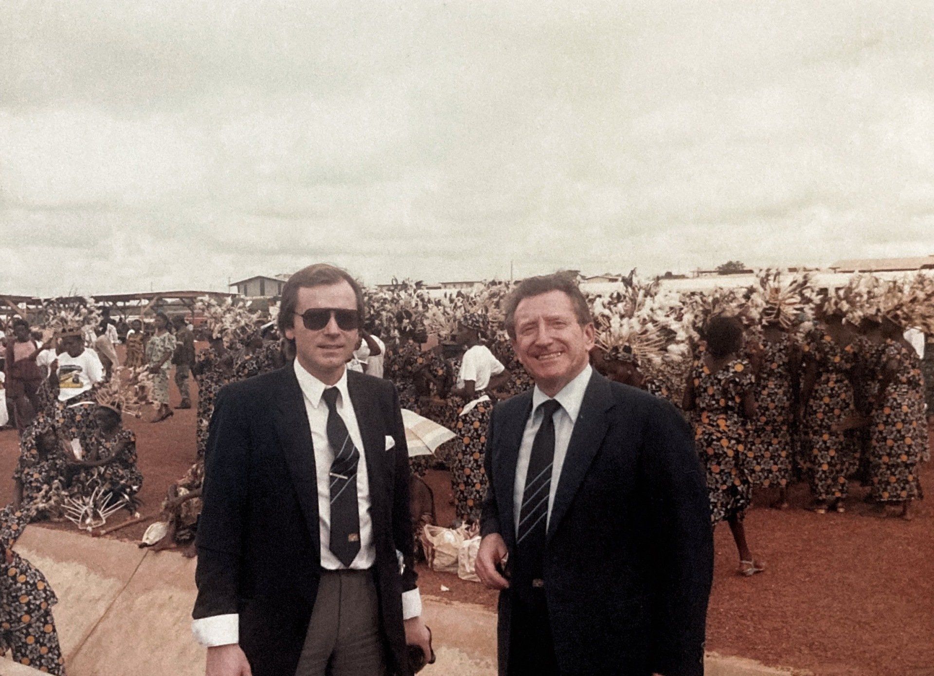 Zwei Männer in Anzug und Krawatte stehen vor einer Menschenmenge