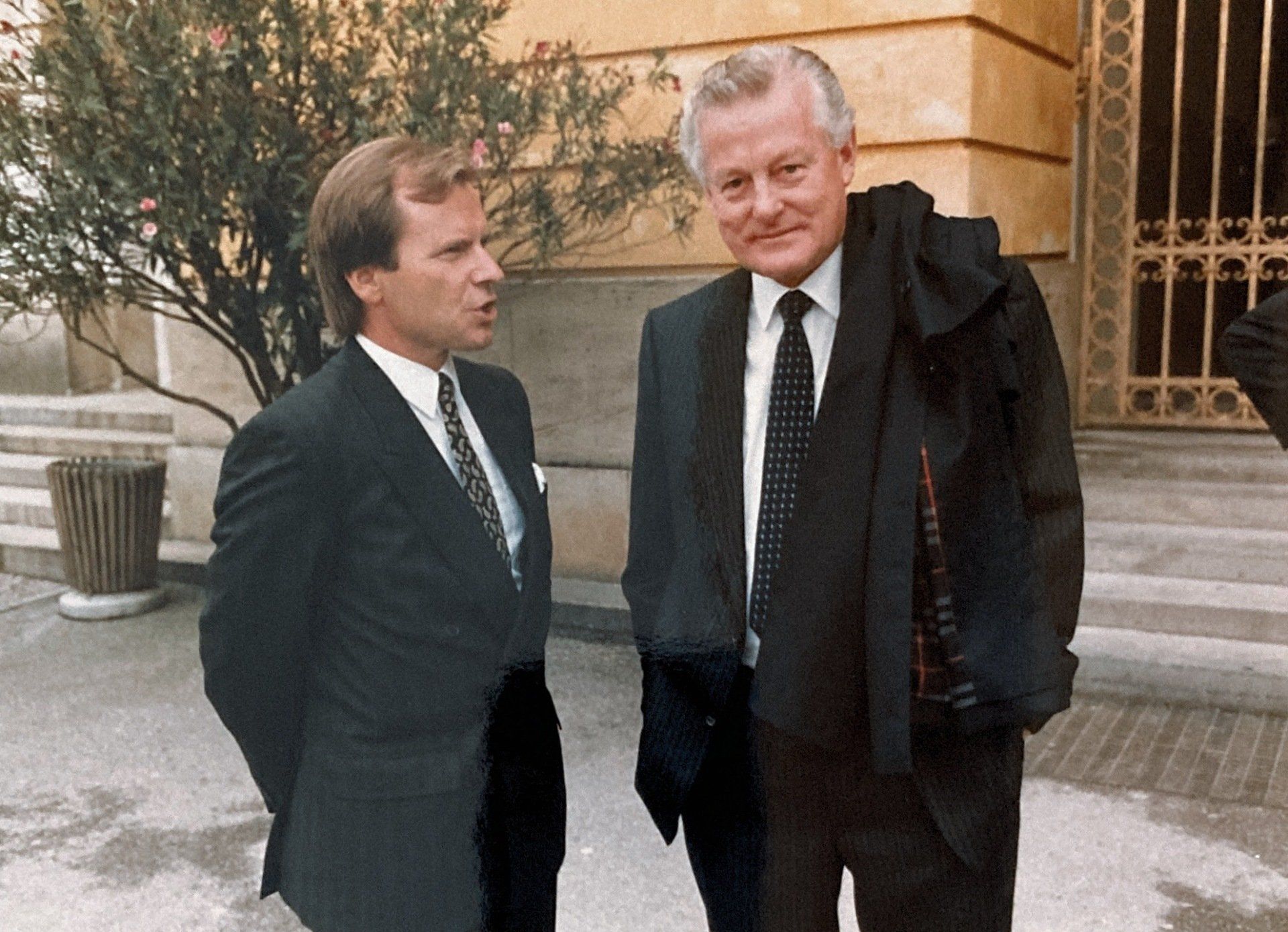 Zwei Männer in Anzug und Krawatte stehen vor einem Gebäude