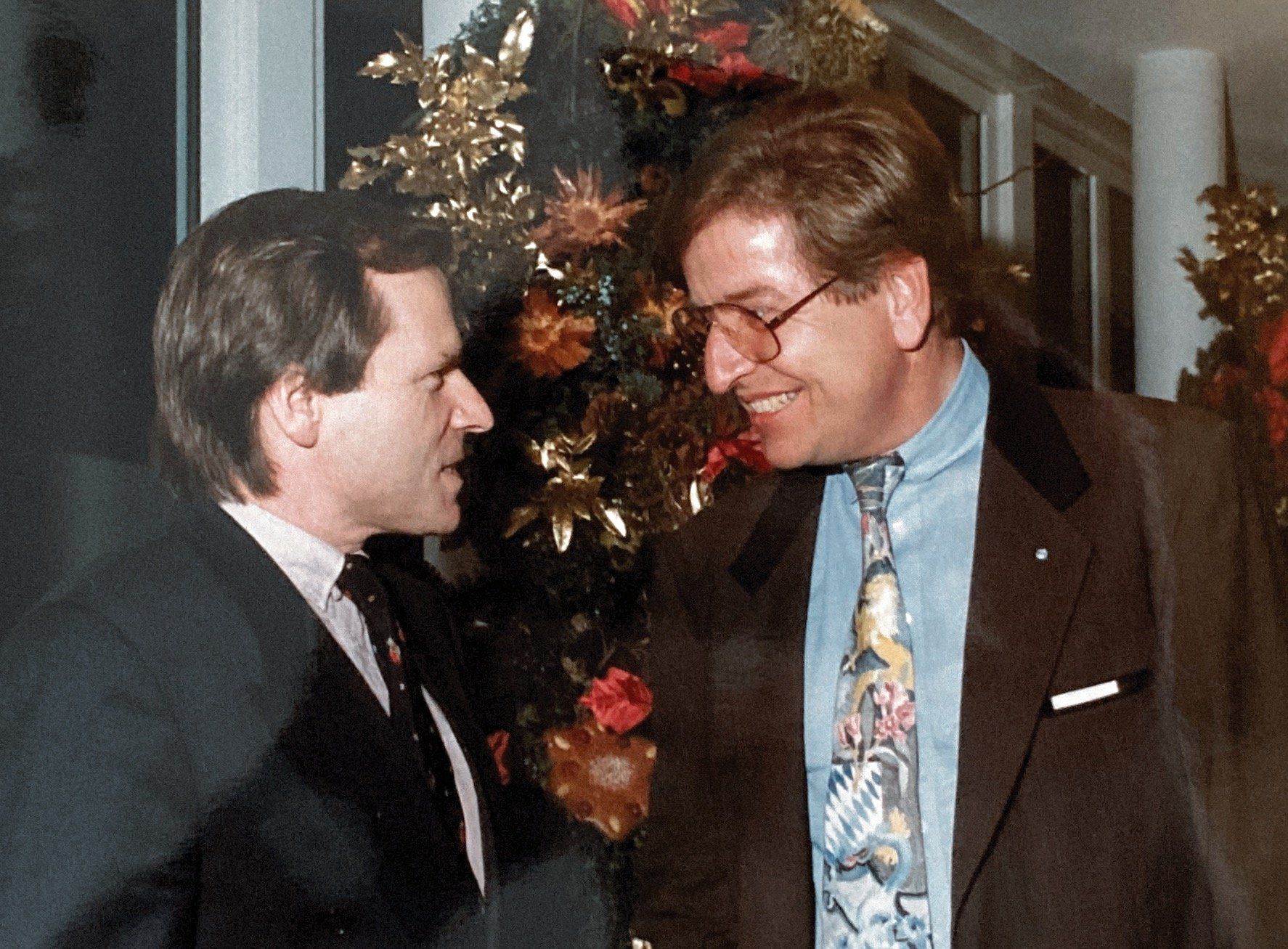 Zwei Männer in Anzug und Krawatte unterhalten sich vor einem Weihnachtsbaum