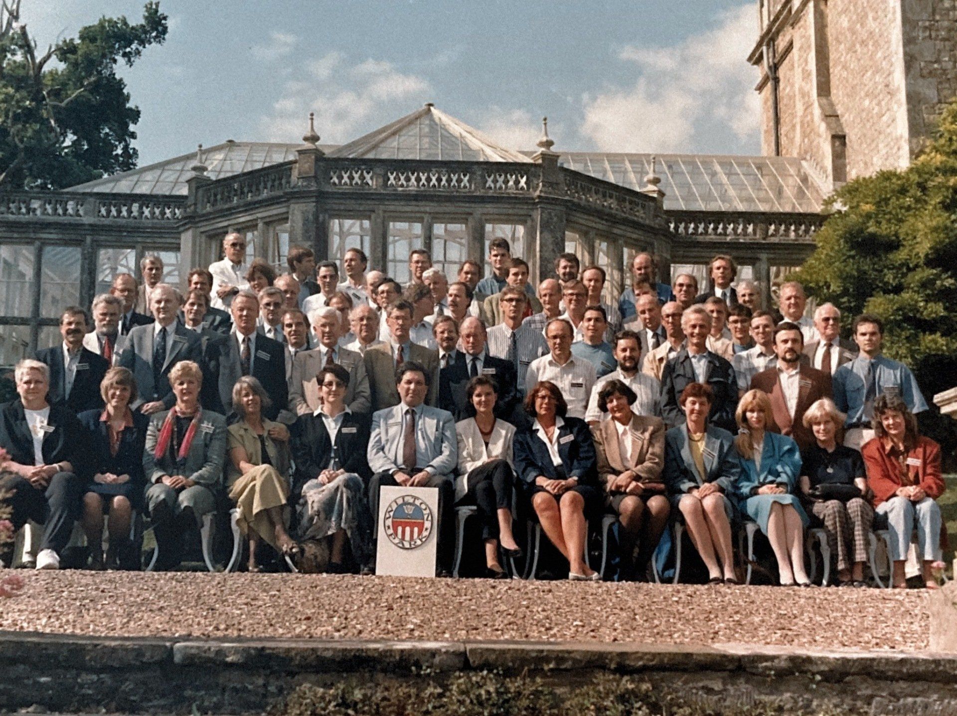 Eine große Gruppe von Menschen posiert für ein Foto vor einem Gebäude, auf dem das Wort „Gesellschaft“ steht
