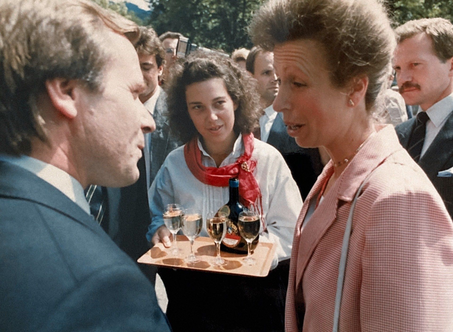 Eine Frau in einer rosa Jacke hält ein Tablett mit Weingläsern