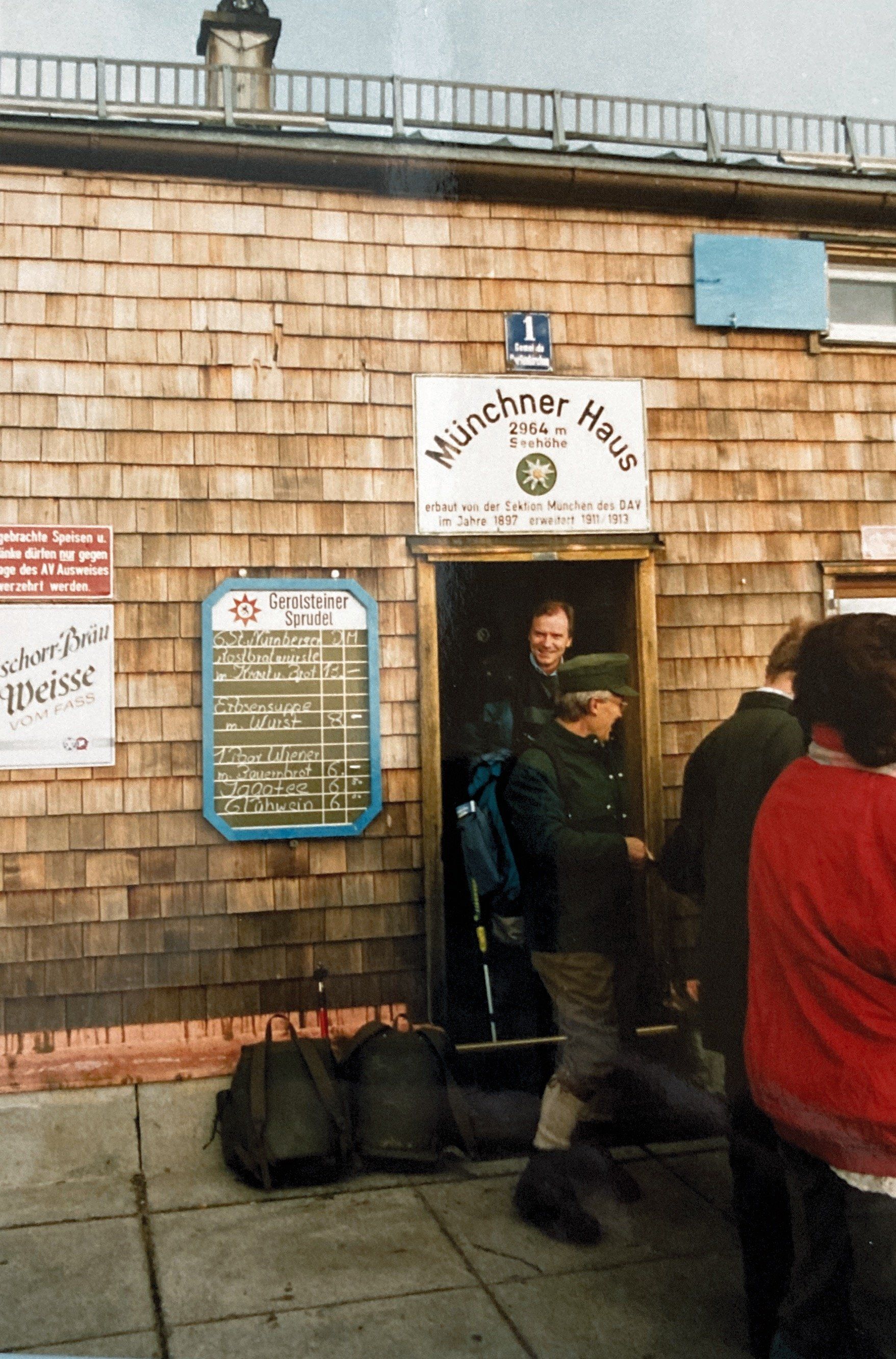 Eine Gruppe von Menschen steht vor einem Gebäude mit der Aufschrift „Münchner Haus“