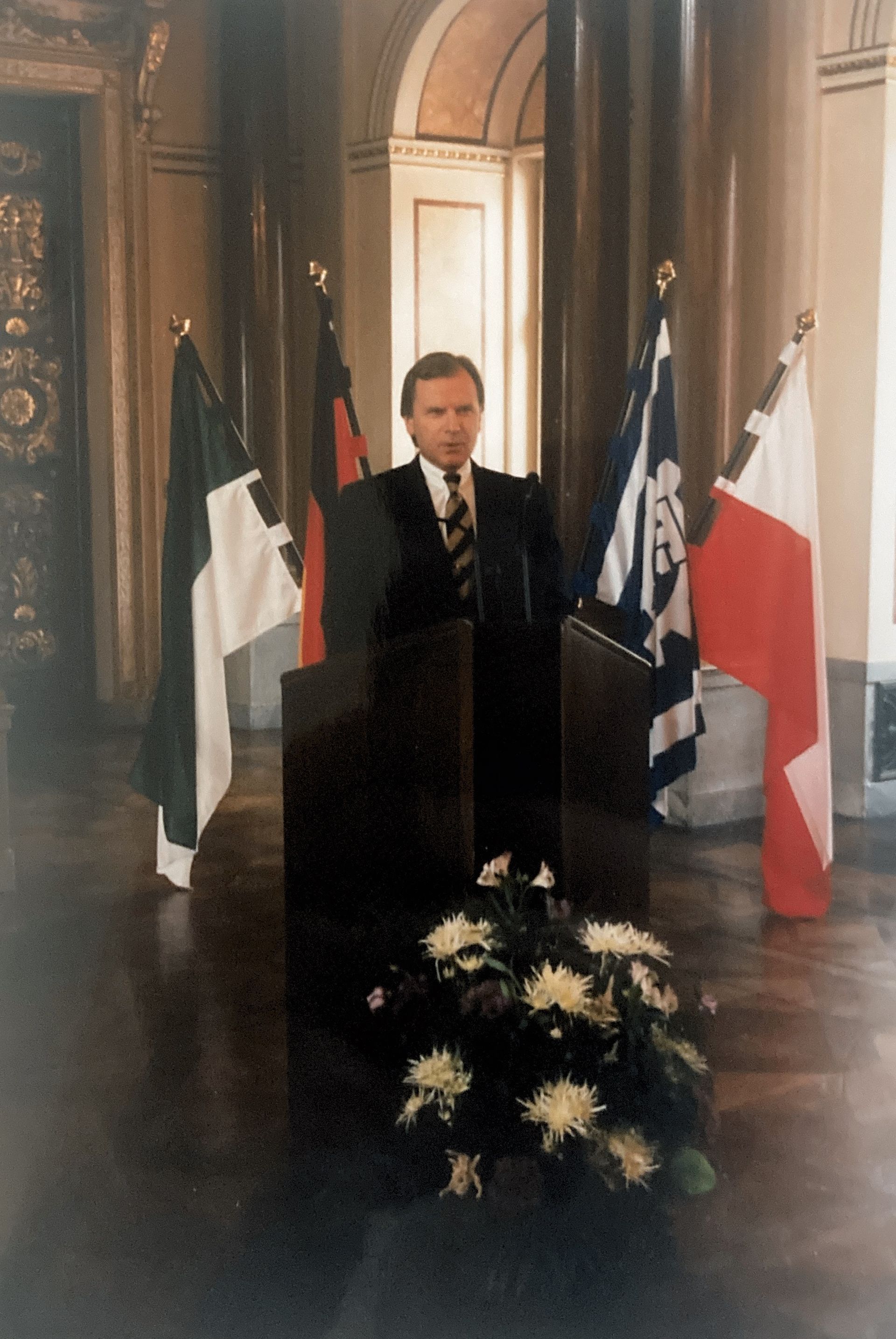 Ein Mann steht auf einem Podium mit Flaggen im Hintergrund