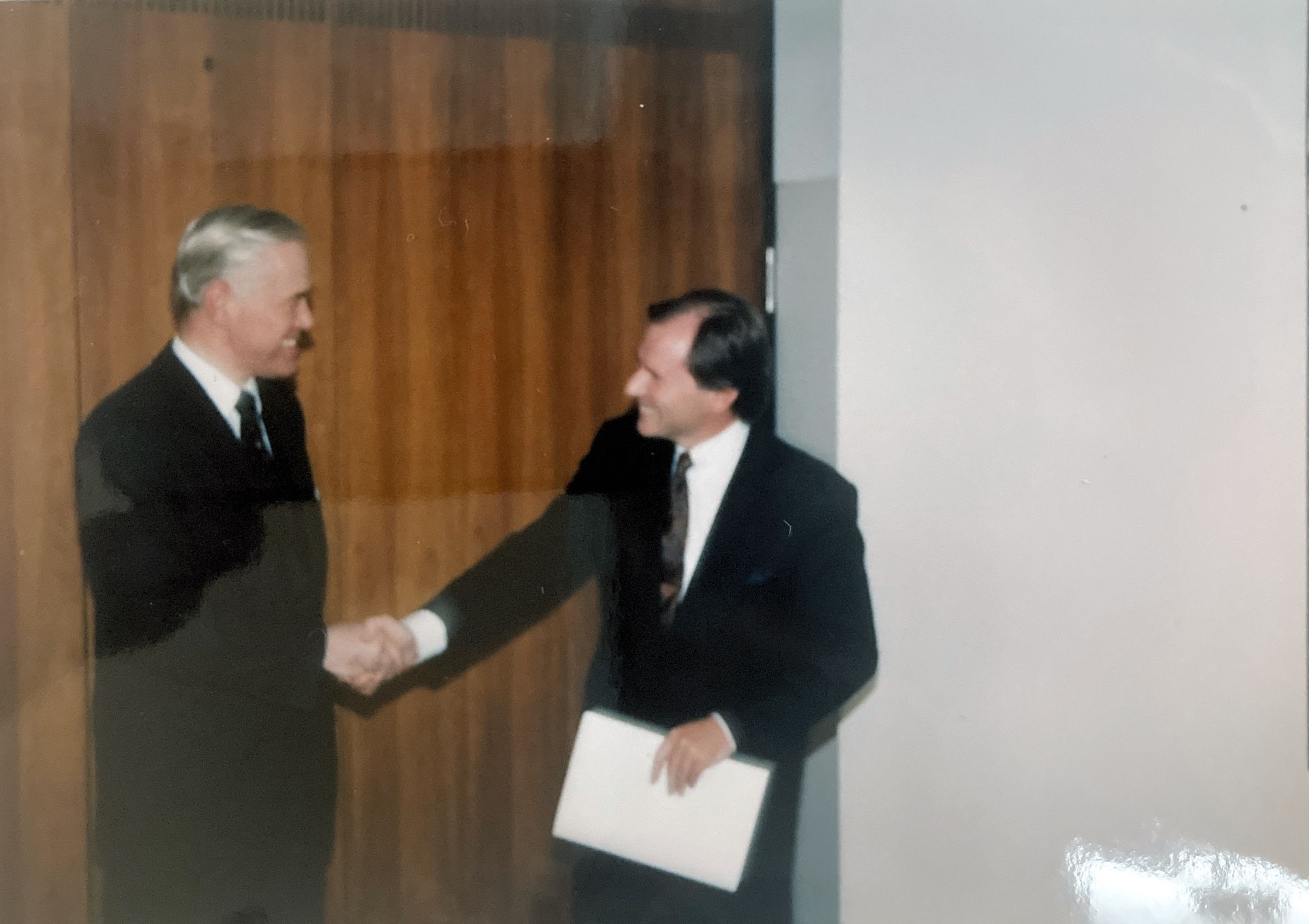 Zwei Männer schütteln sich die Hände, einer hält ein Stück Papier in der Hand