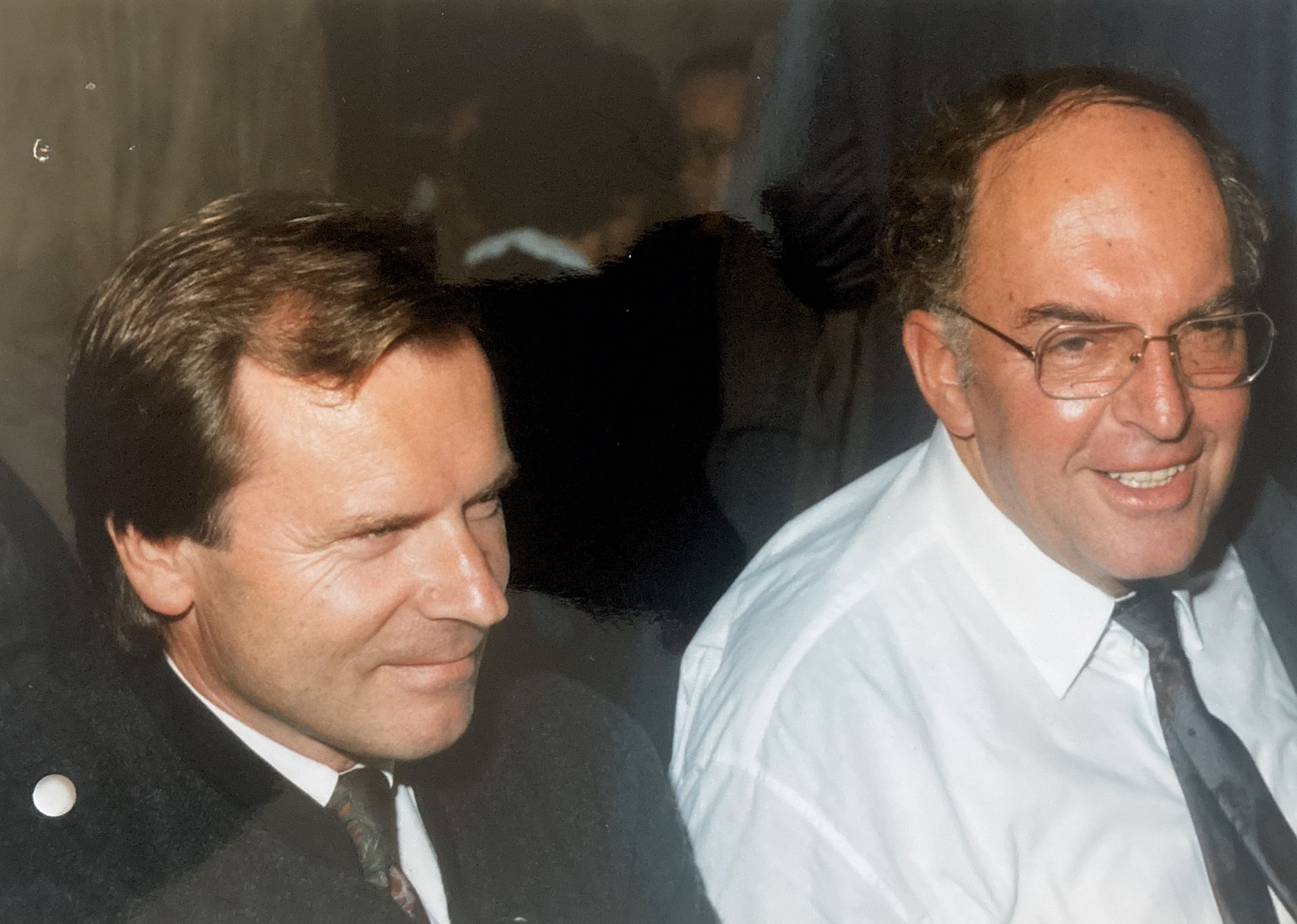 Zwei Männer sitzen nebeneinander und lächeln in die Kamera