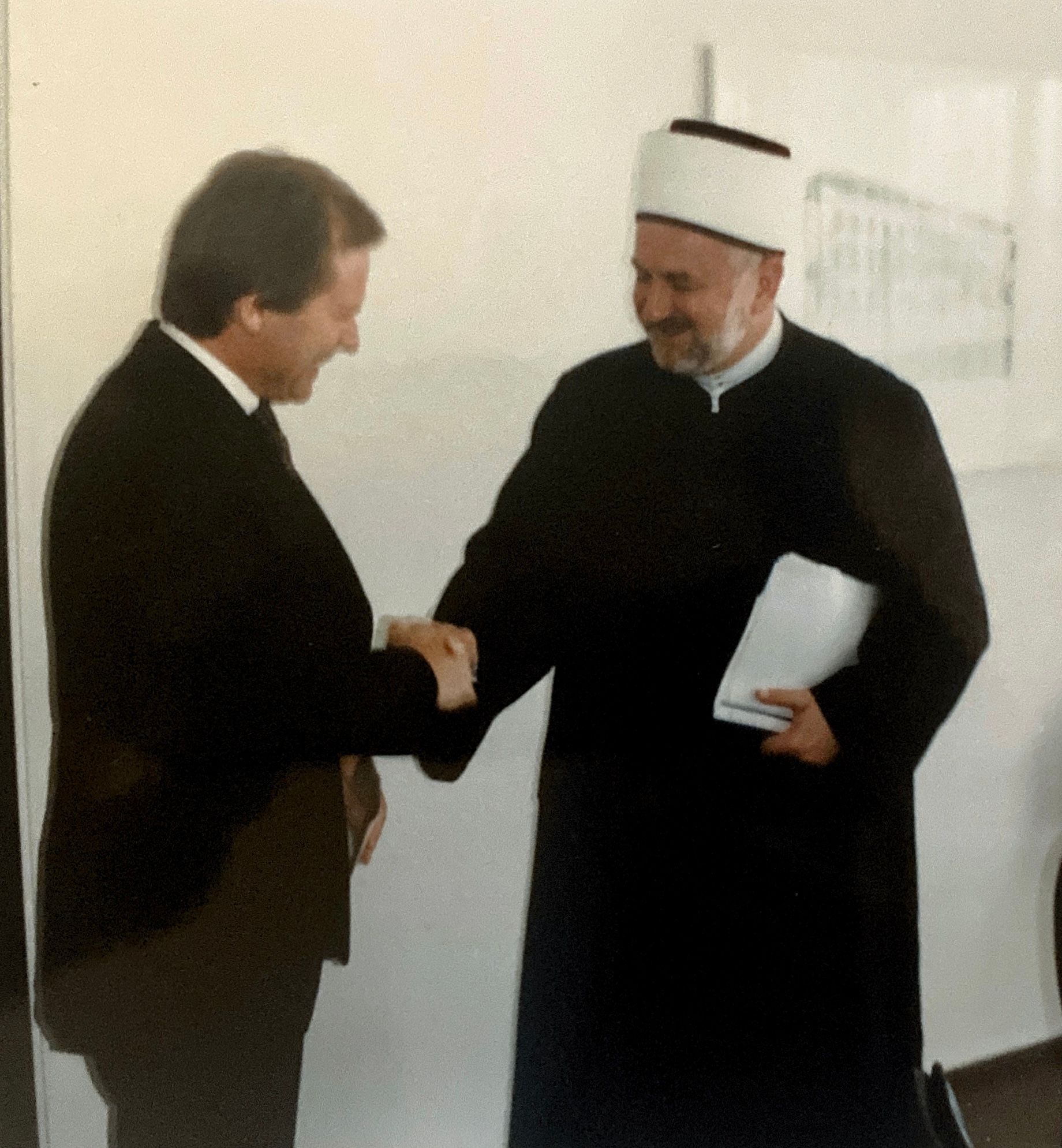 Zwei Männer schütteln sich vor einer weißen Wand die Hände