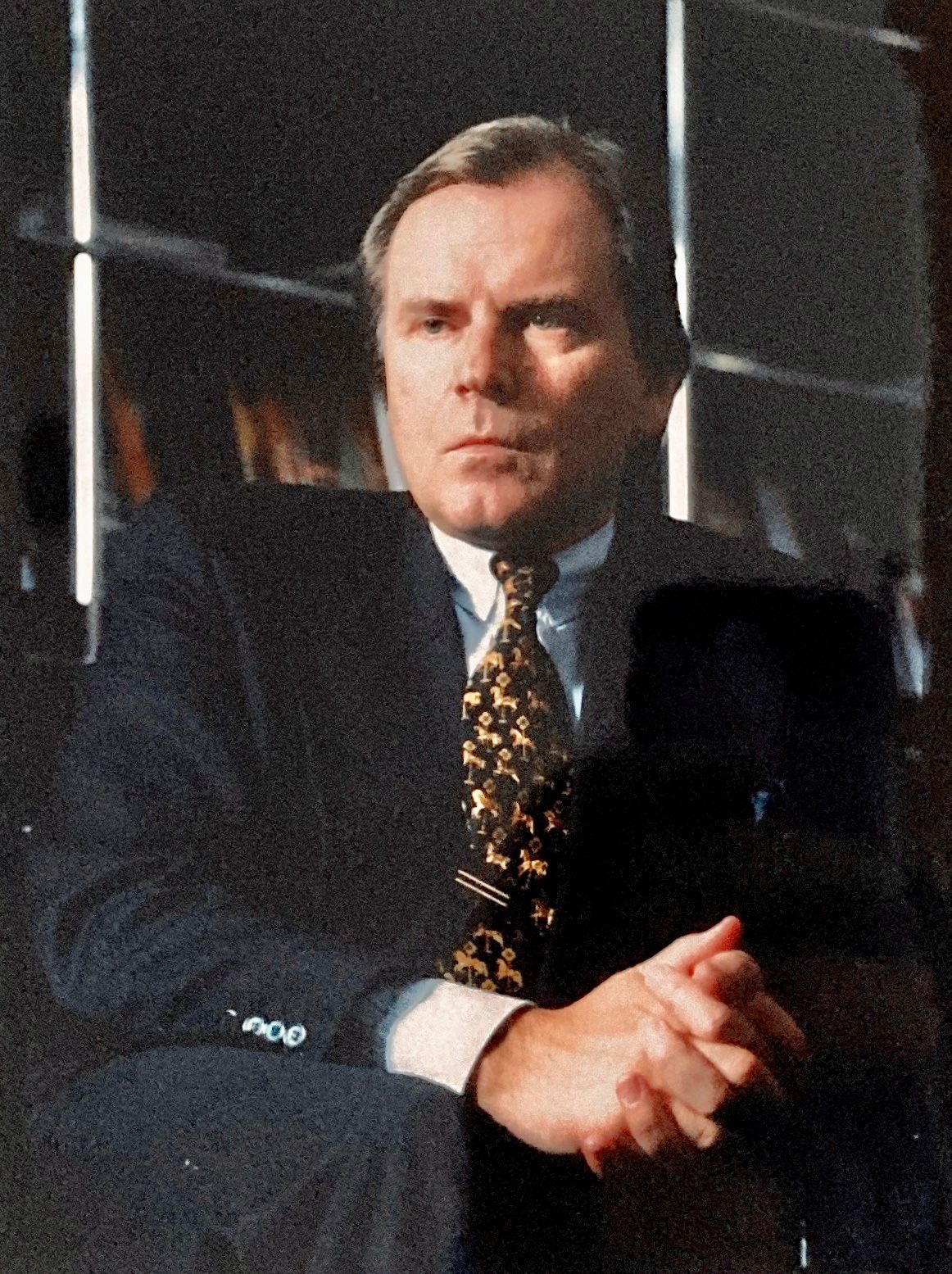 Ein Mann in Anzug und Krawatte sitzt mit gefalteten Händen da