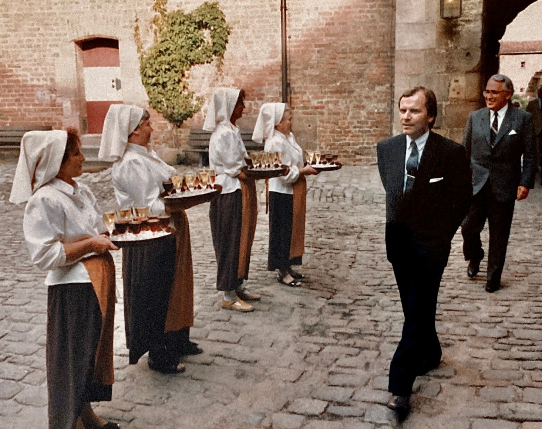 Ein Mann im Anzug geht an einer Gruppe von Frauen vorbei, die Tabletts mit Essen tragen