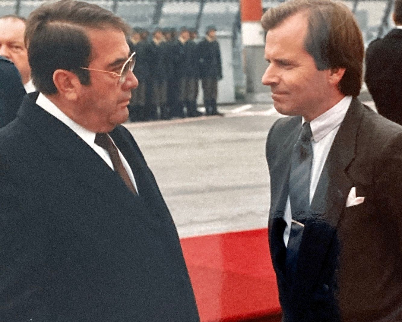 Zwei Männer in Anzügen stehen nebeneinander auf einem roten Teppich