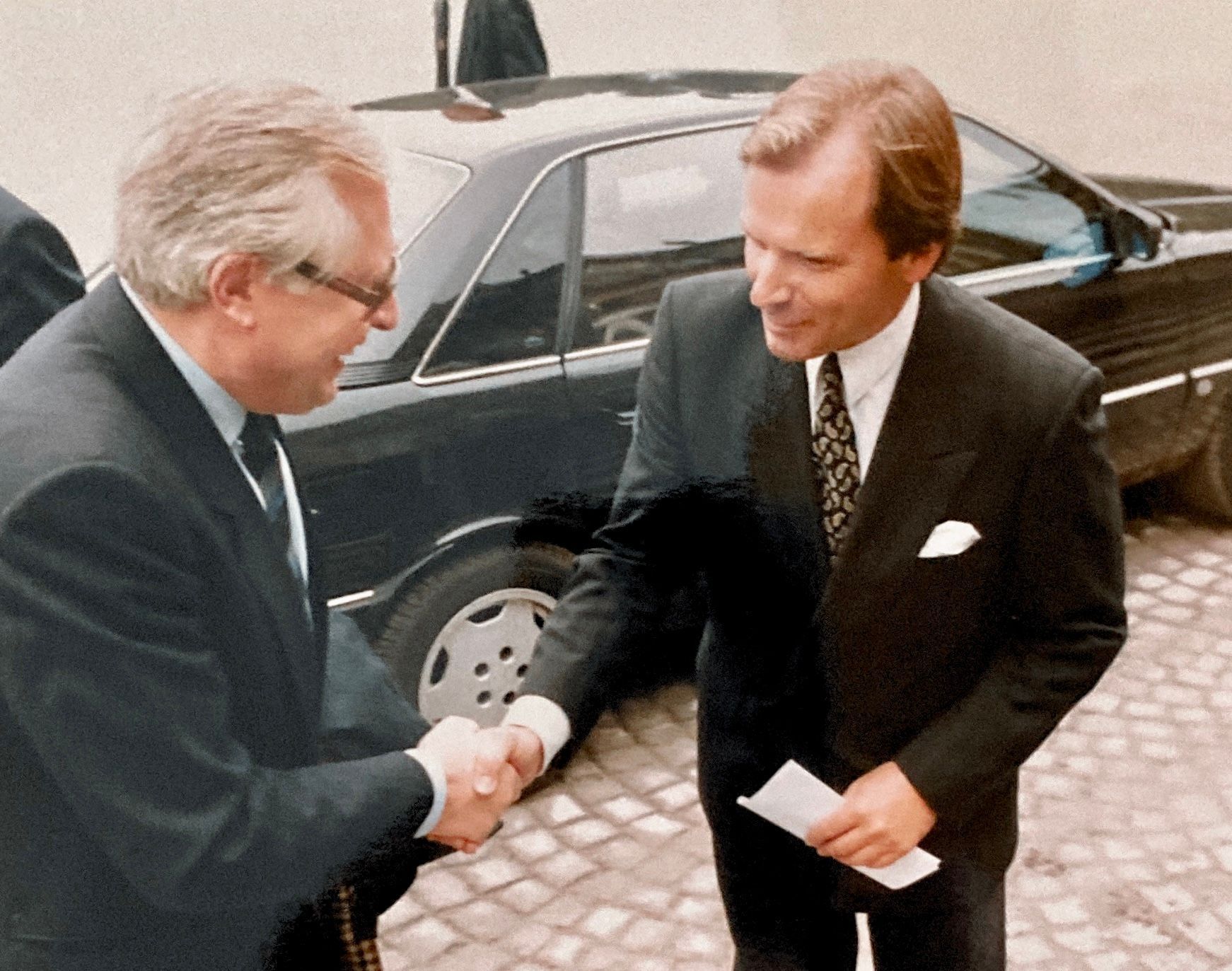 Zwei Männer schütteln sich vor einem schwarzen Auto die Hände