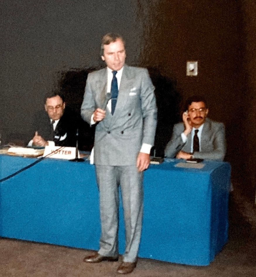 Ein Mann im Anzug steht vor einem blauen Tisch mit einem Schild mit der Aufschrift „Potter“