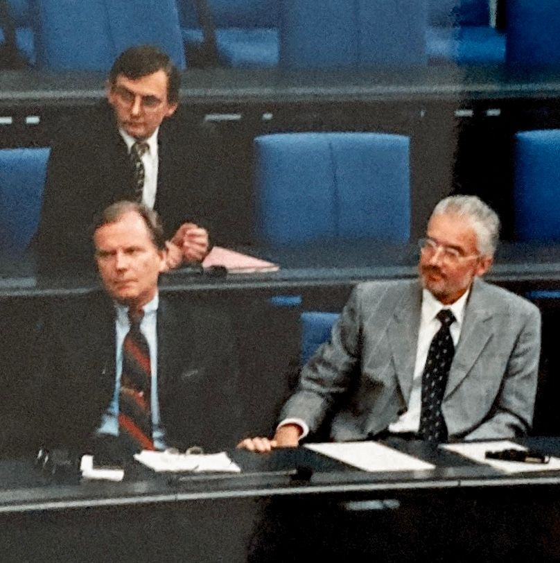 Drei Männer in Anzug und Krawatte sitzen an einem Tisch