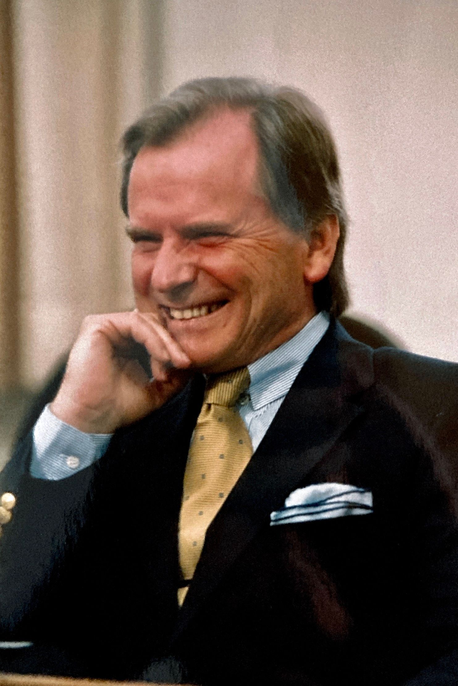 Ein Mann in Anzug und Krawatte lächelt und legt die Hand auf sein Kinn.