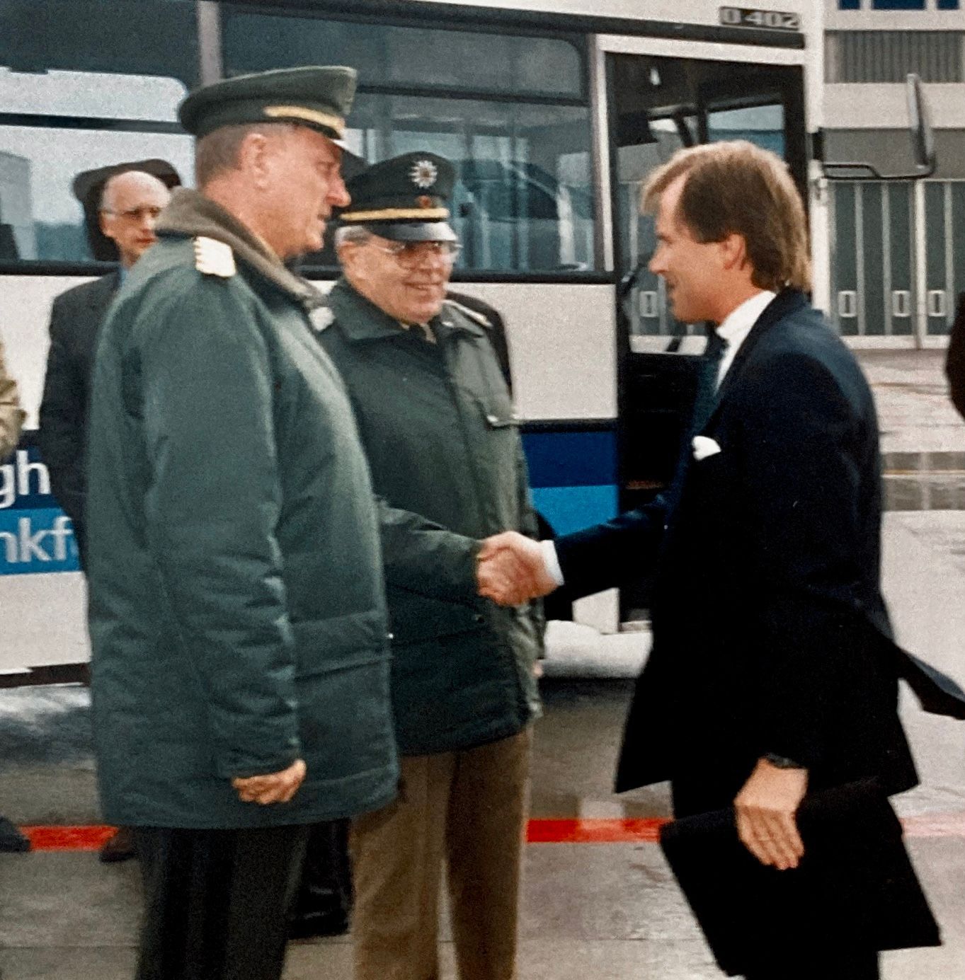 Eine Gruppe von Männern schüttelt sich vor einem Bus mit der Aufschrift NKF die Hände