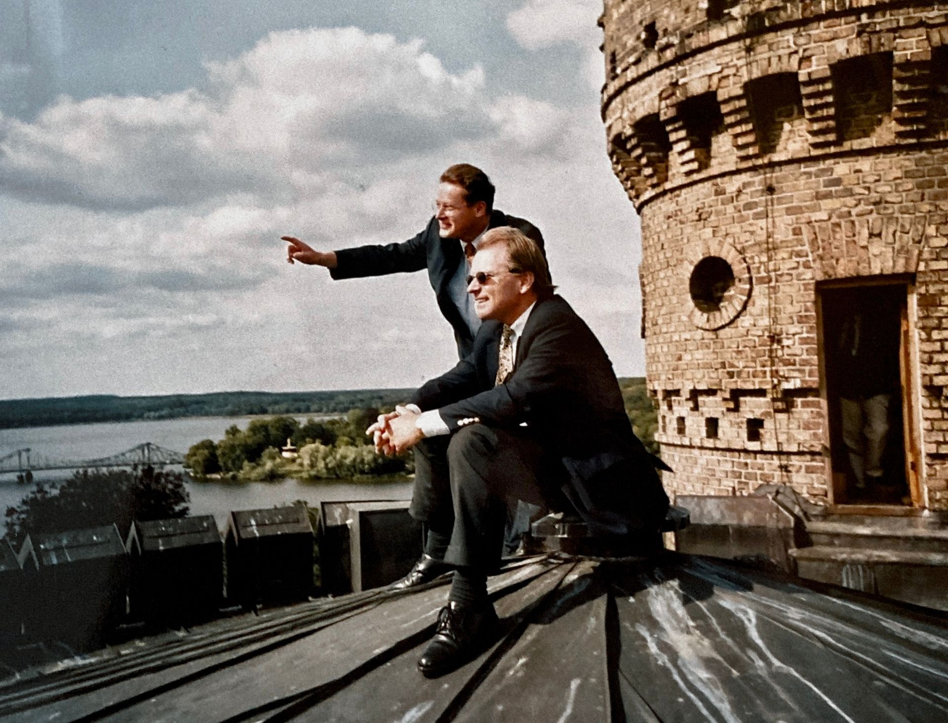 Zwei Männer sitzen auf dem Dach eines Gebäudes mit Blick auf ein Gewässer