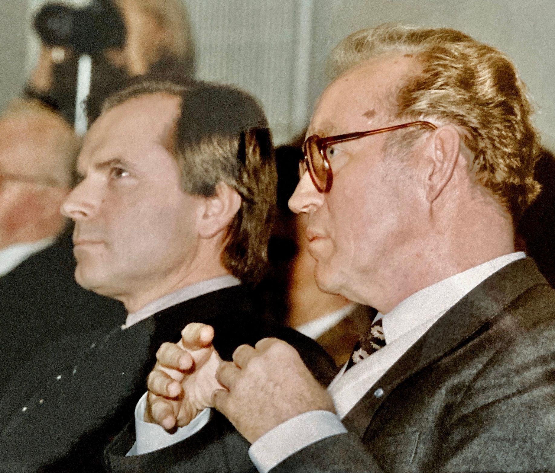 Ein Mann mit Brille sitzt neben einem anderen Mann im Anzug