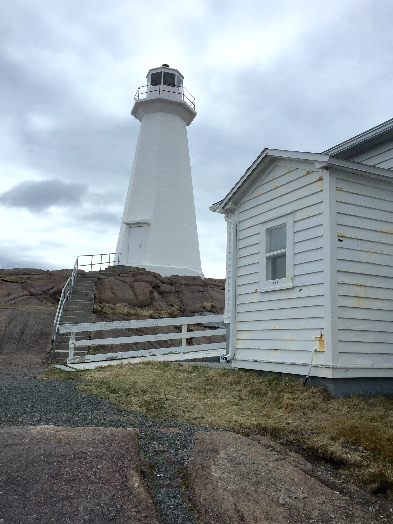 Ein weißer Leuchtturm steht auf einem felsigen Hügel neben einem weißen Haus.