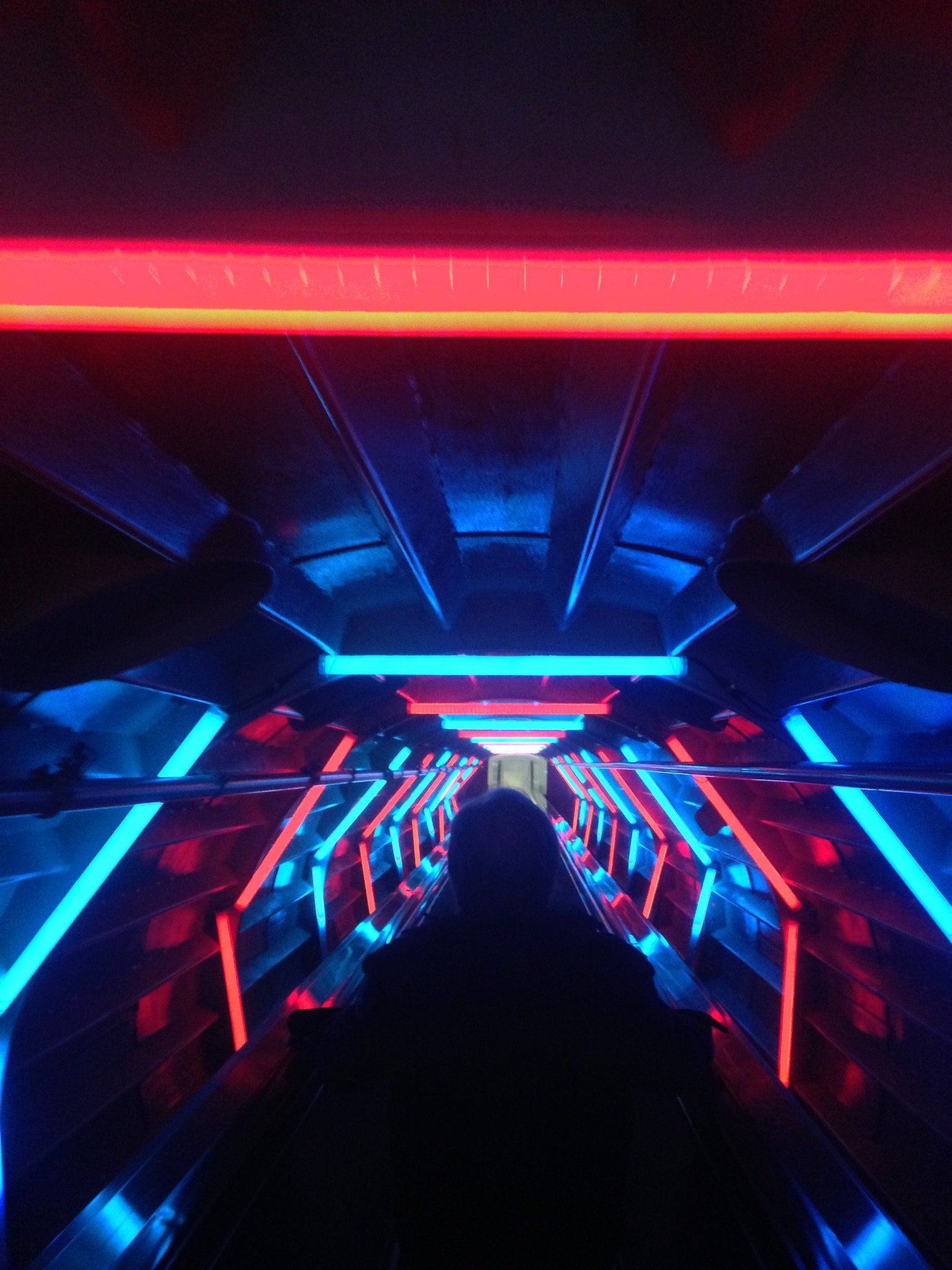 Eine Person fährt auf einer Rolltreppe in einem dunklen Raum mit Neonlicht.