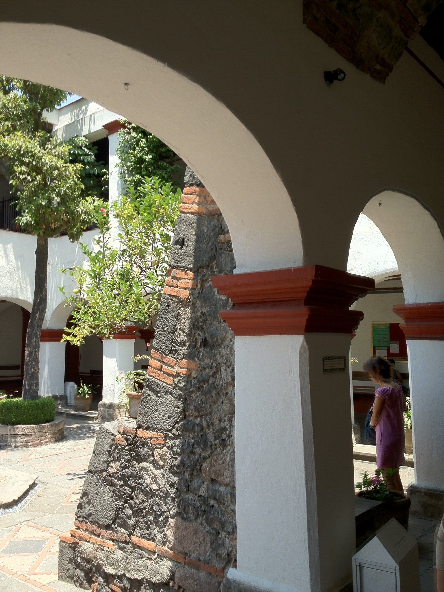 Eine Frau in einem rosa Kleid steht zwischen zwei Bögen in einem Innenhof