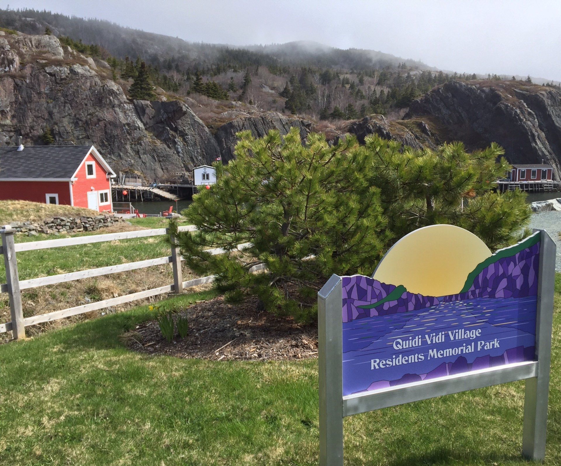 Ein Schild vor einem Zaun mit einem roten Haus im Hintergrund