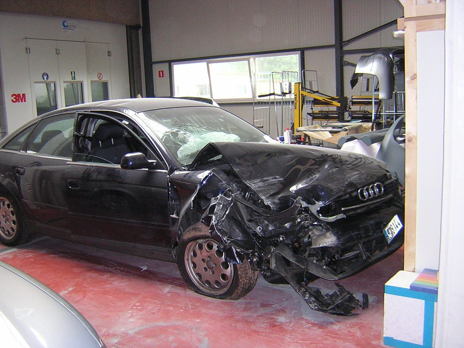 Ein schwarzes Auto mit beschädigter Frontpartie steht in einer Garage