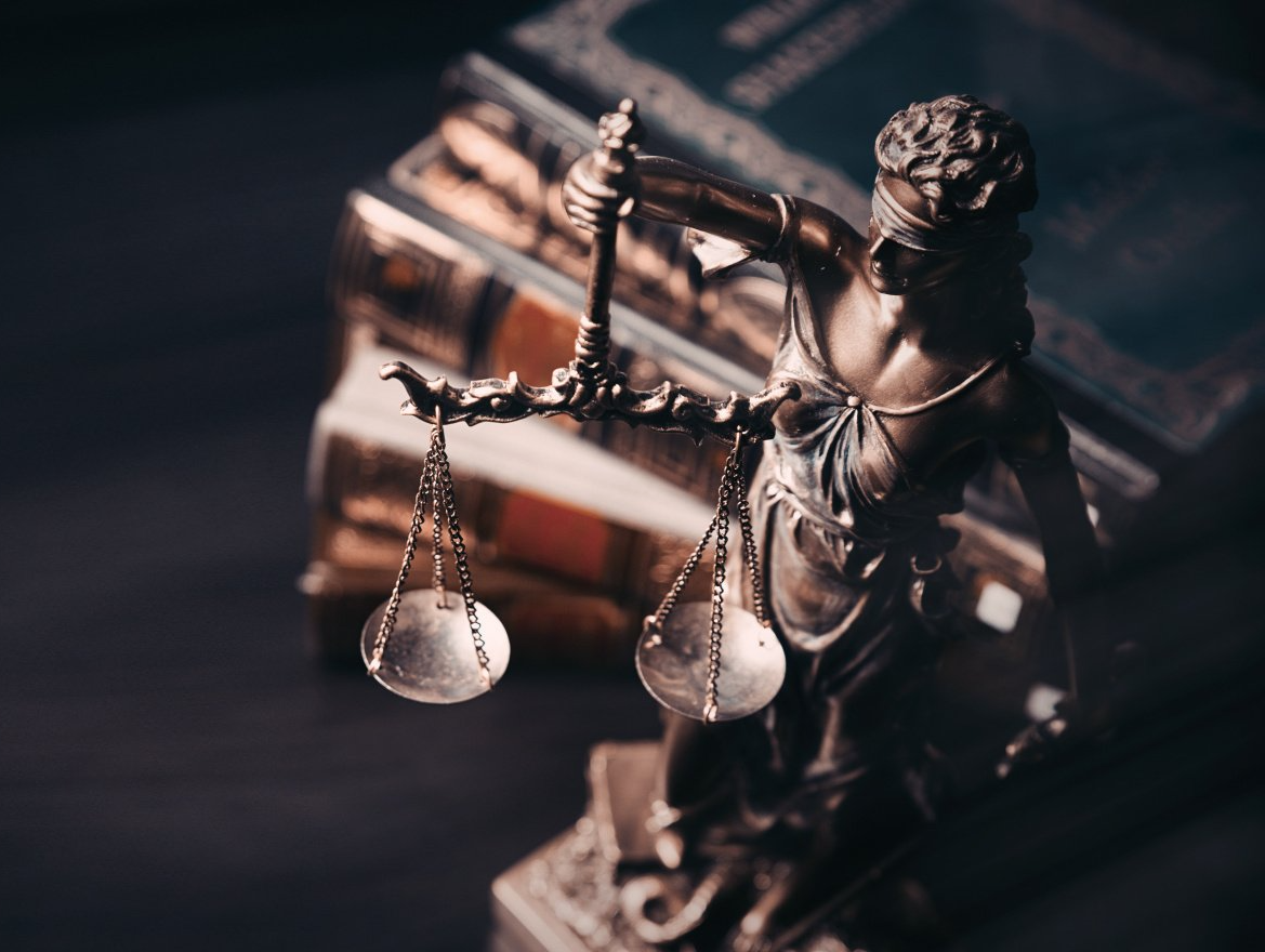 Eine Statue der Gerechtigkeit, die vor einem Stapel Bücher eine Waage hält.