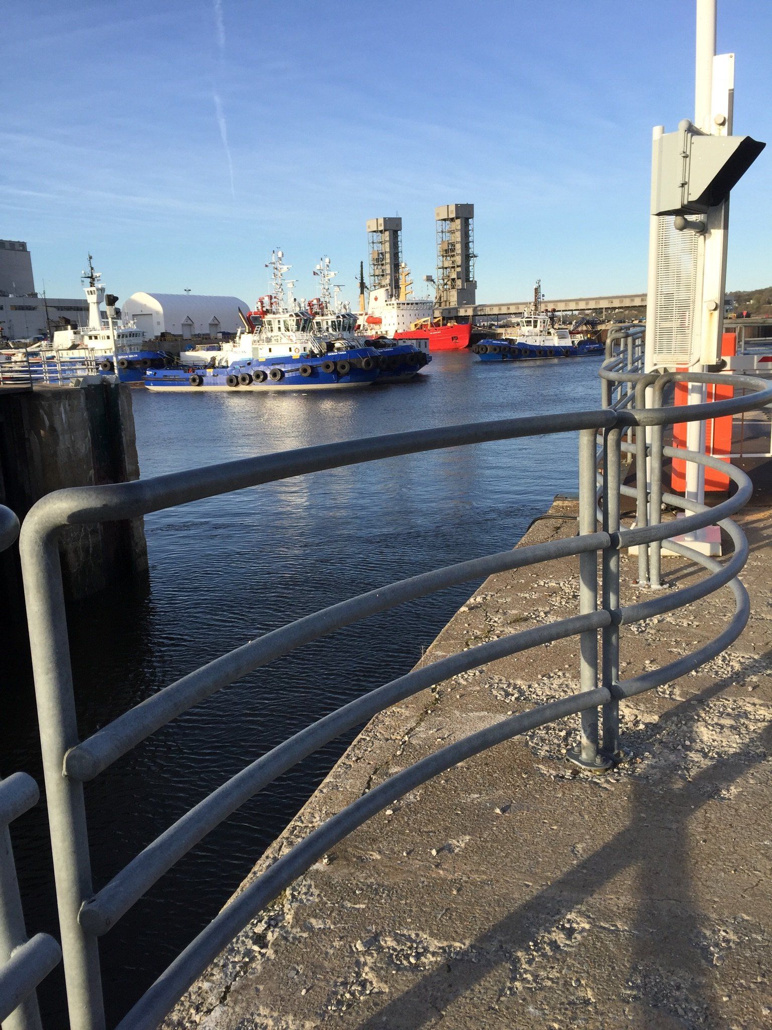 Ein Zaun umgibt ein Gewässer mit Booten im Hintergrund.