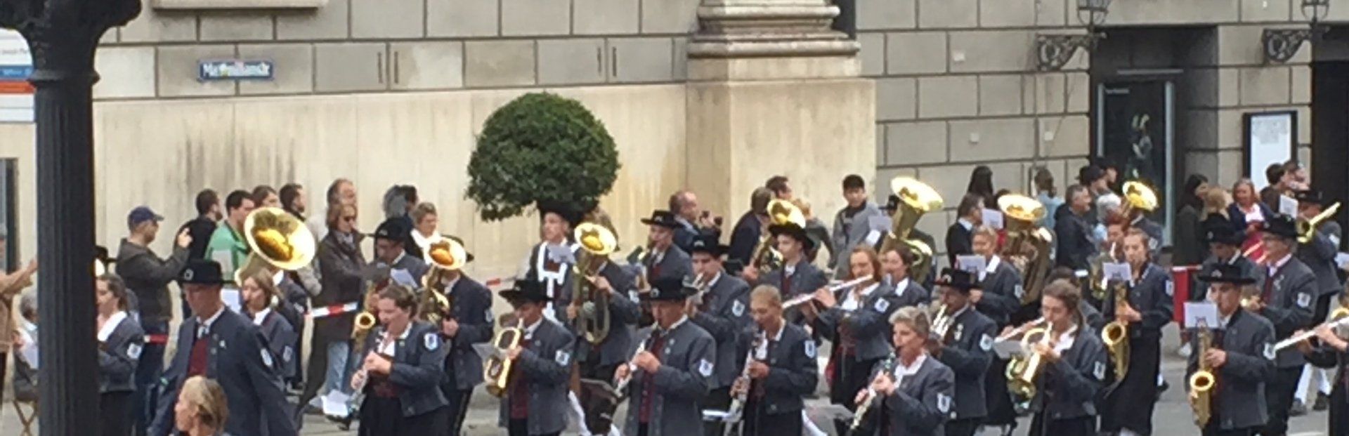 Eine große Band marschiert vor einem Gebäude eine Straße entlang.