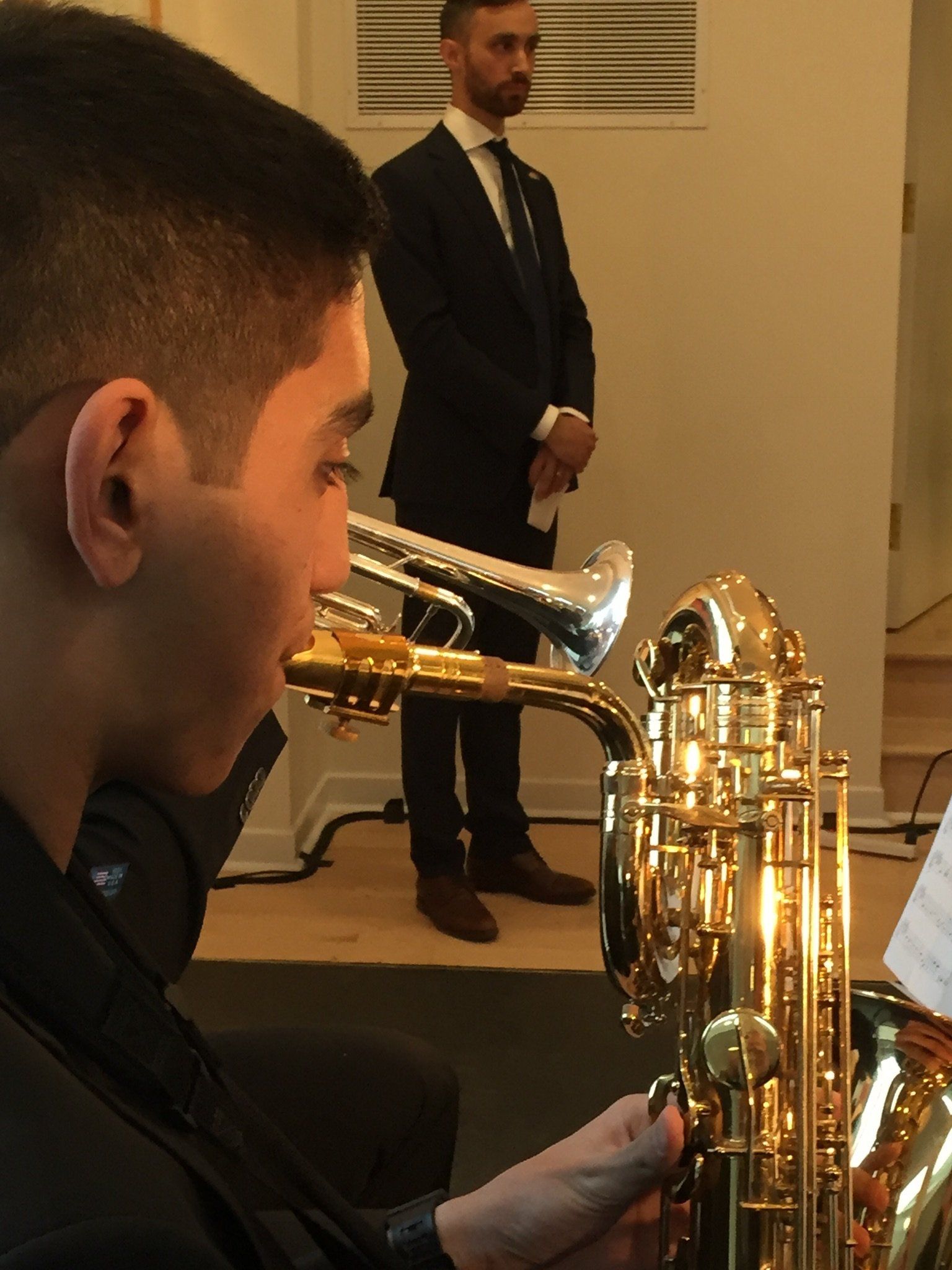 Ein Mann im Anzug steht hinter einem Mann, der Saxophon spielt