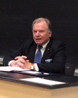 Ein Mann in Anzug und Krawatte sitzt mit gefalteten Händen an einem Schreibtisch