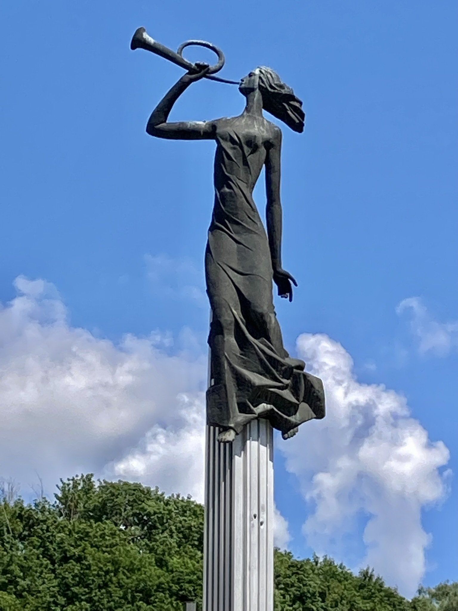 Eine Statue einer Frau, die auf einer Stange eine Trompete bläst.