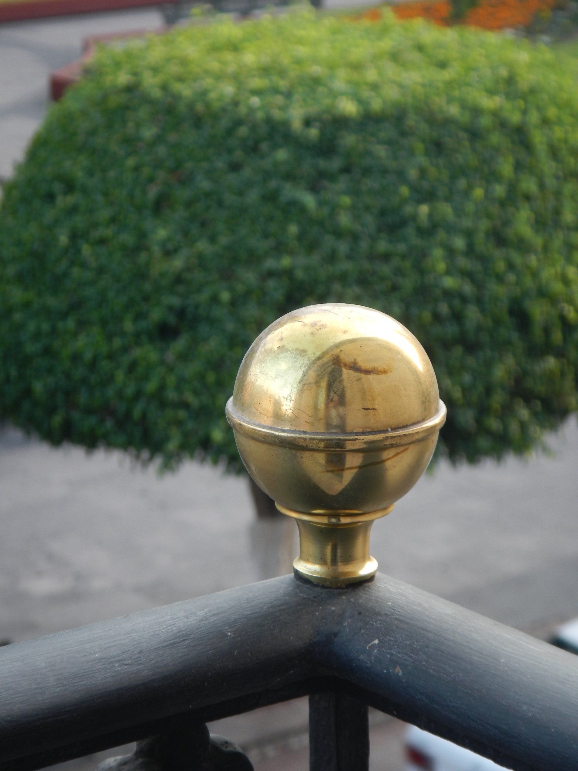 Eine Messingkugel auf einem Geländer mit einem Busch im Hintergrund