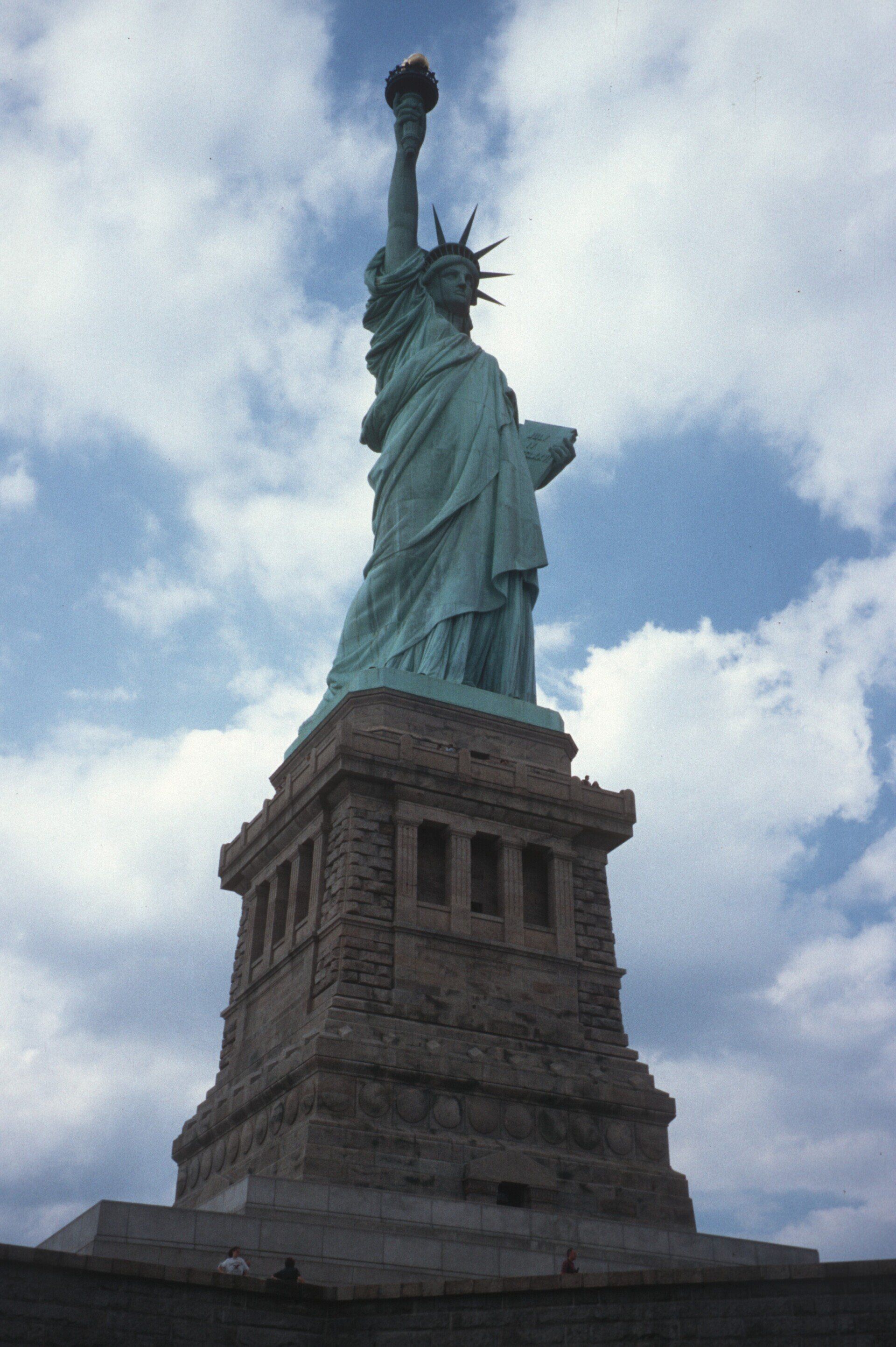 Die Freiheitsstatue ragt hoch vor einem bewölkten blauen Himmel empor