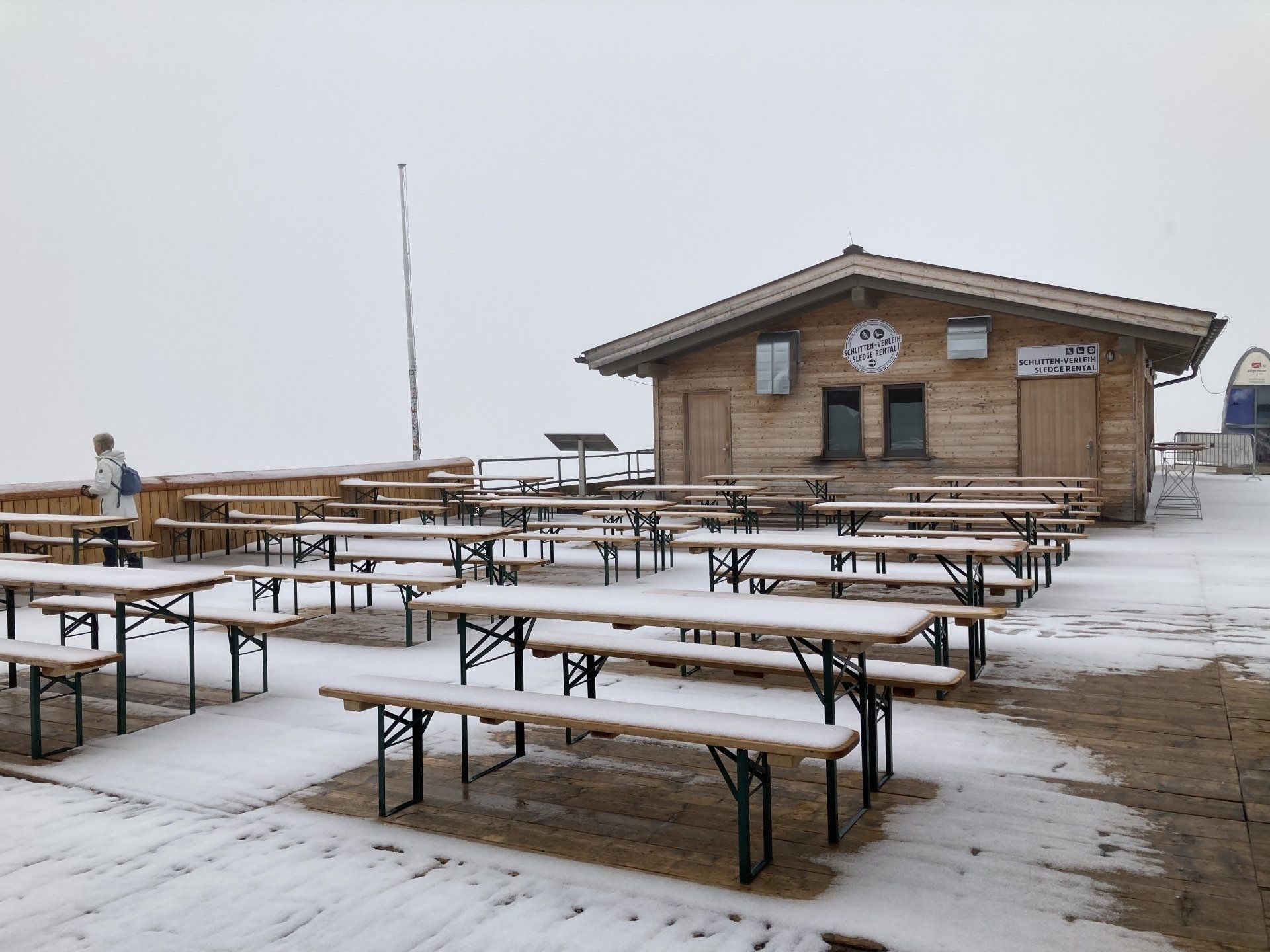 Eine Reihe schneebedeckter Picknicktische vor einem Holzgebäude.