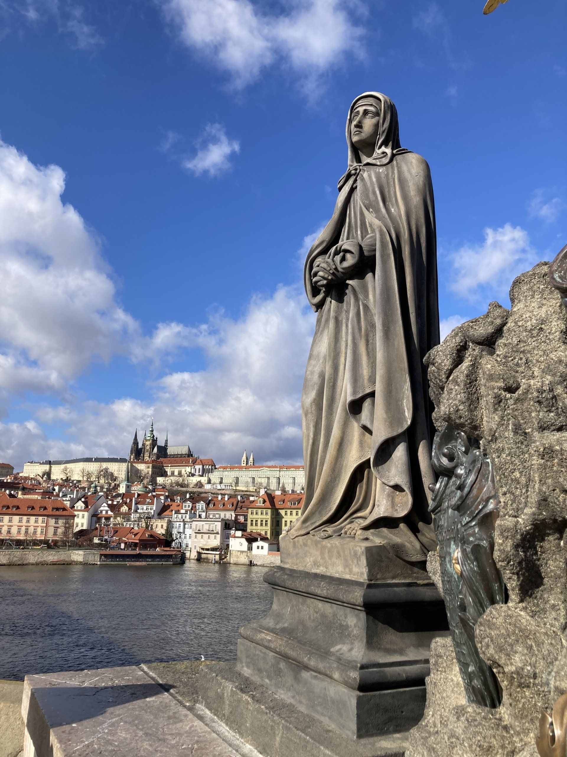 Eine Statue einer Frau, die neben einem Fluss steht, im Hintergrund eine Stadt.
