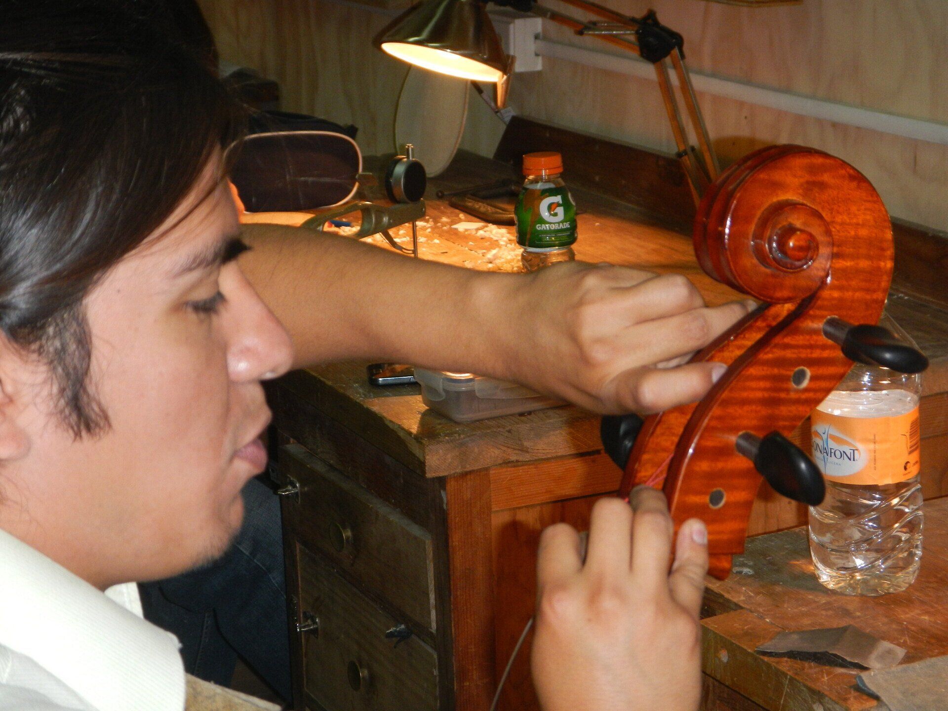 Ein Mann arbeitet an einem Cello neben einer Flasche Gatorade