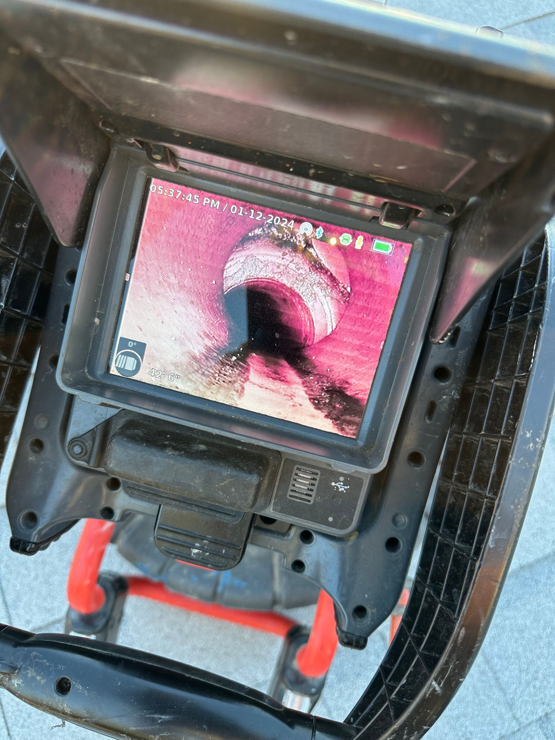 Screen of a pipe inspection camera showing a sewer line with rust-colored walls.