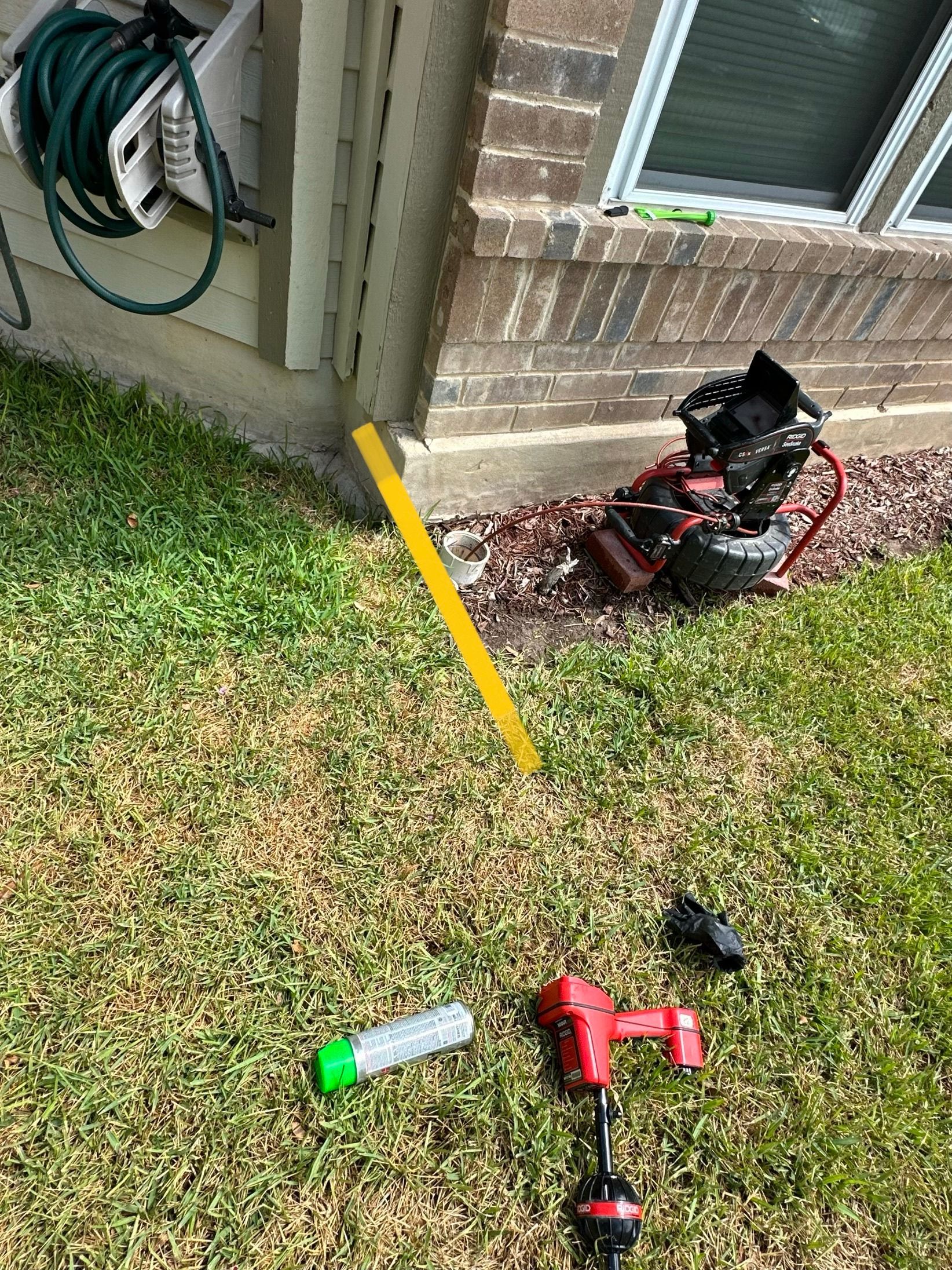 Green grass, a yellow level, and red tools near a building corner.