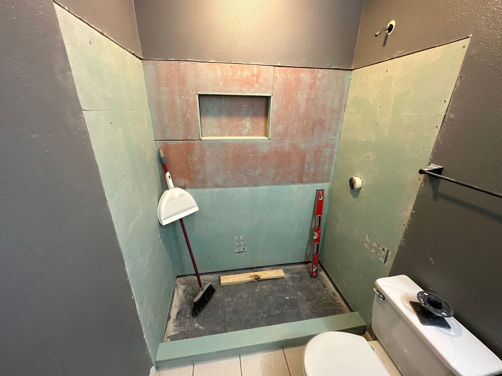 Bathroom under renovation with green cement board on walls, red in the niche, and a toilet visible.