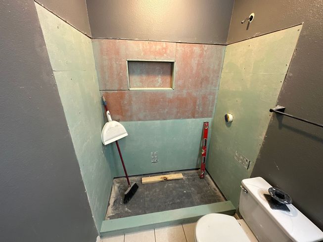 Bathroom under renovation with green cement board on walls, red in the niche, and a toilet visible.