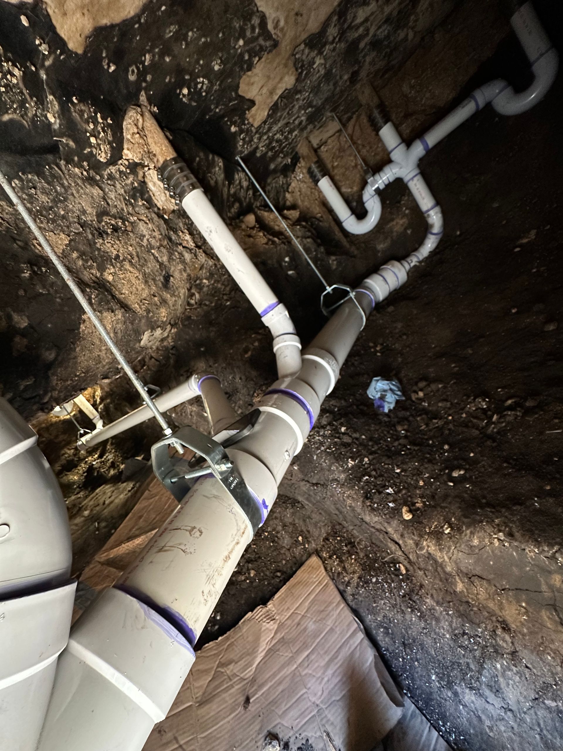 Plumbing pipes in a confined space; gray PVC, white tape, and metal straps.