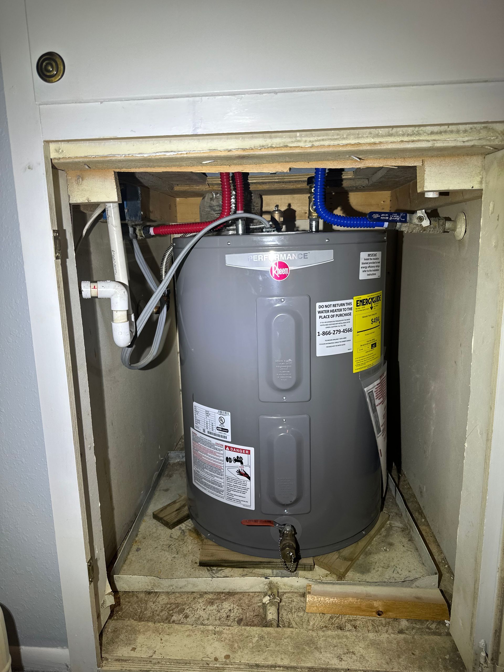 Water heater inside a wooden cabinet, with red/blue pipes.