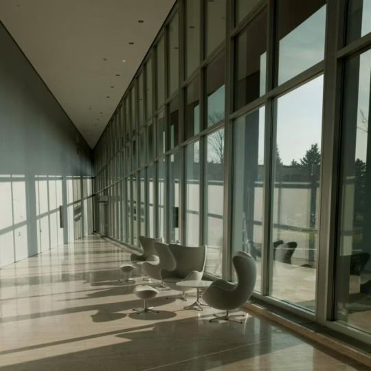 Empty modern hallway with floor-to-ceiling windows and sculptural white chairs in sunlight