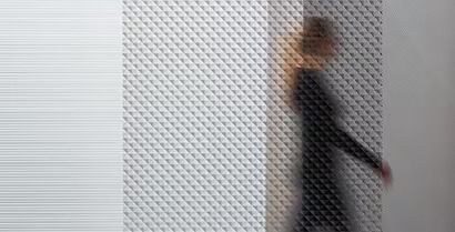 Blurred person in dark clothing walking past a textured white and gray wall.